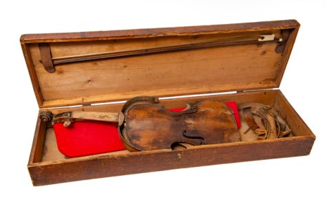 Jamie Macpherson’s broken fiddle, displayed in an open wooden case lined with red fabric.